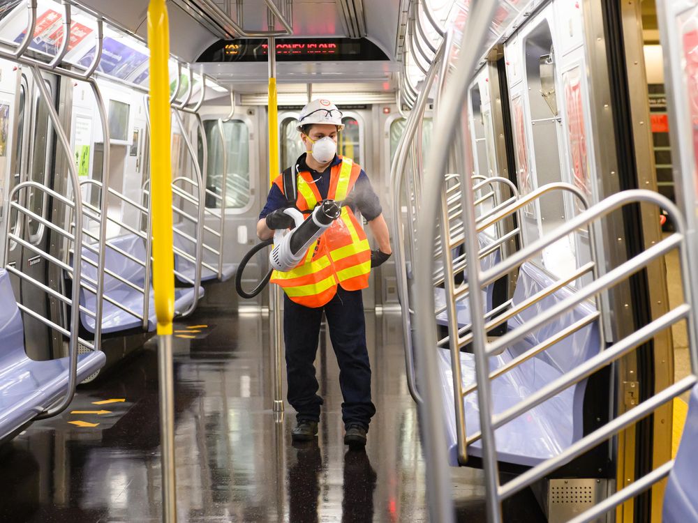 MTA worker wearing hard hat, mask, and safety vest uses a bulk disinfectant machine to deep clean an MTA subway car