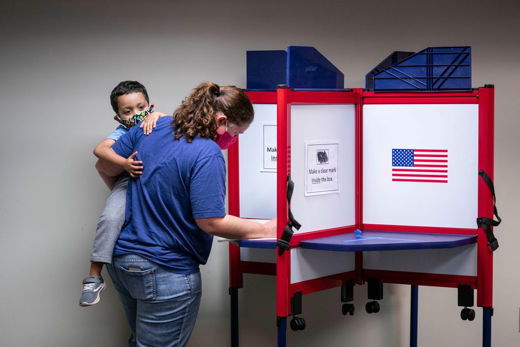 woman holding child and voting, both wearing masks
