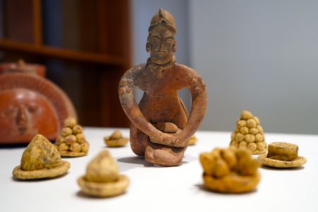 A Oaxacan figure is depicted making masa with a metate, a stone tool used for grinding corn.