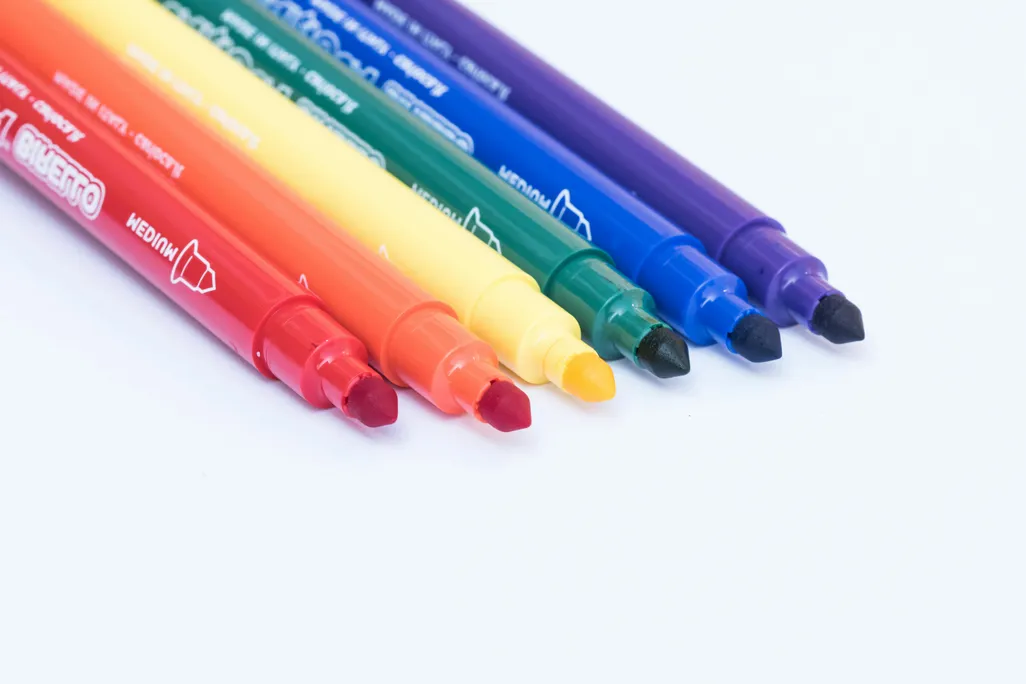 six markers in the colors of a rainbow sit on a white surface