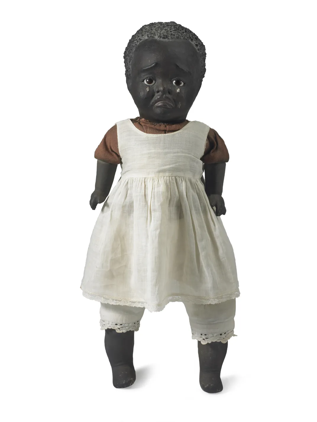 A baby doll modeled to resemble a Black baby, with a white pinafore and tears rolling down its cheeks