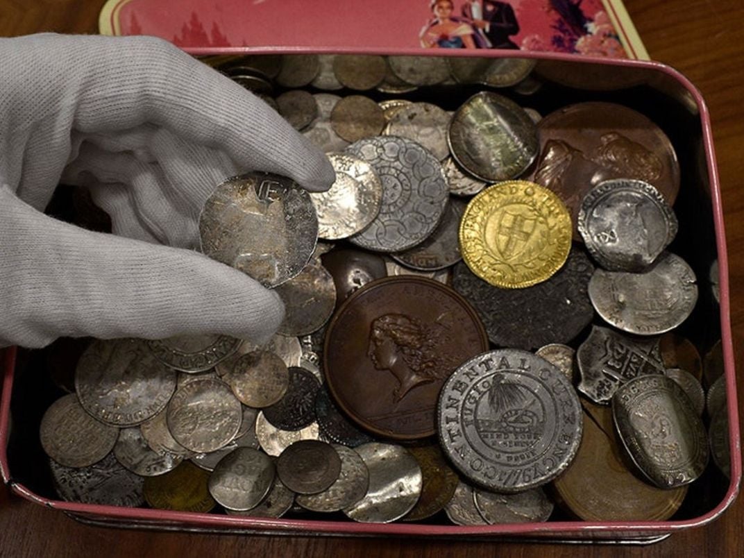 The New England coin held over the tin with assorted old coins