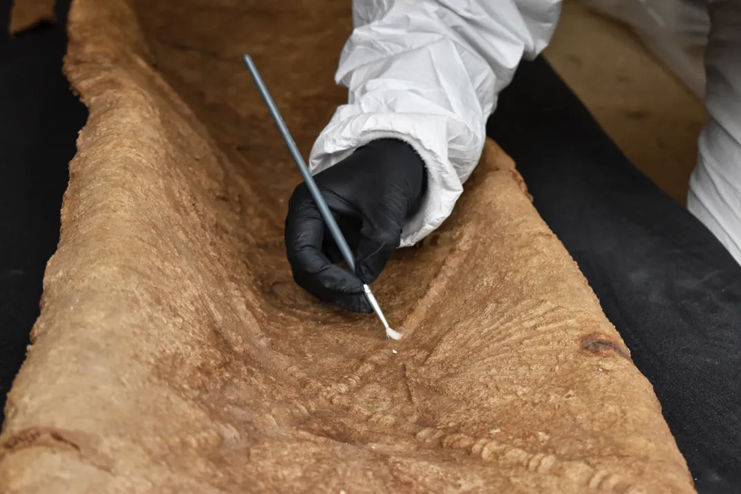 Gloved hand using an instrument to clean a lead coffin