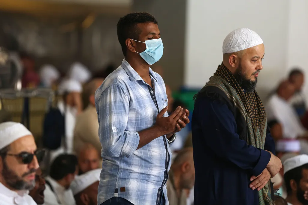 Muslim men pray at the Grand Mosque, one wearing a mask
