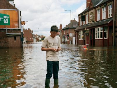 A teenage boy sends a text message on his mobile phone as stands in the floodwater on the main street of Bentley in Doncaster.