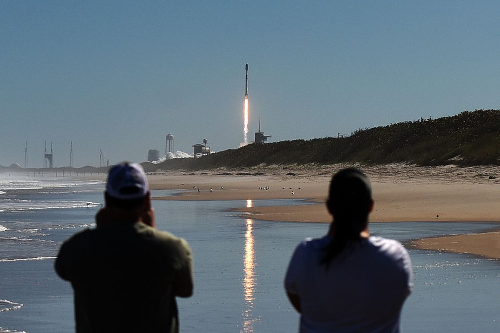 Image of SpaceX’s Falcon 9 rocket lifting off in Florida with blue sky and trail of fire, onlookers in foreground
