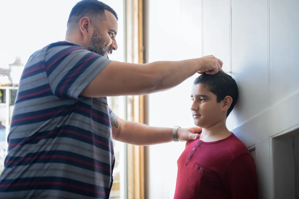 An adult male measuring a younger male child against a wall