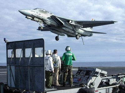 In January 2001, the Landing Signal Officer and other crew on the platform are only a few of the thousands supporting the mission to get this F-14 Tomcat safely aboard the USS Abraham Lincoln.