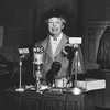 Eleanor Roosevelt standing in front of four microphones labeled as CBS and NBC