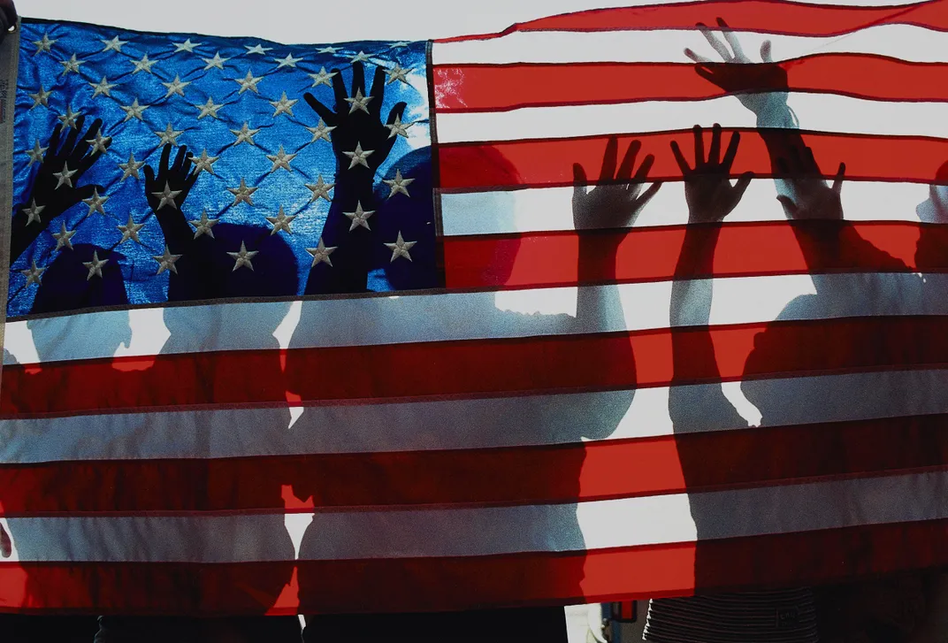 An American flag with the silhouettes of children playing behind it