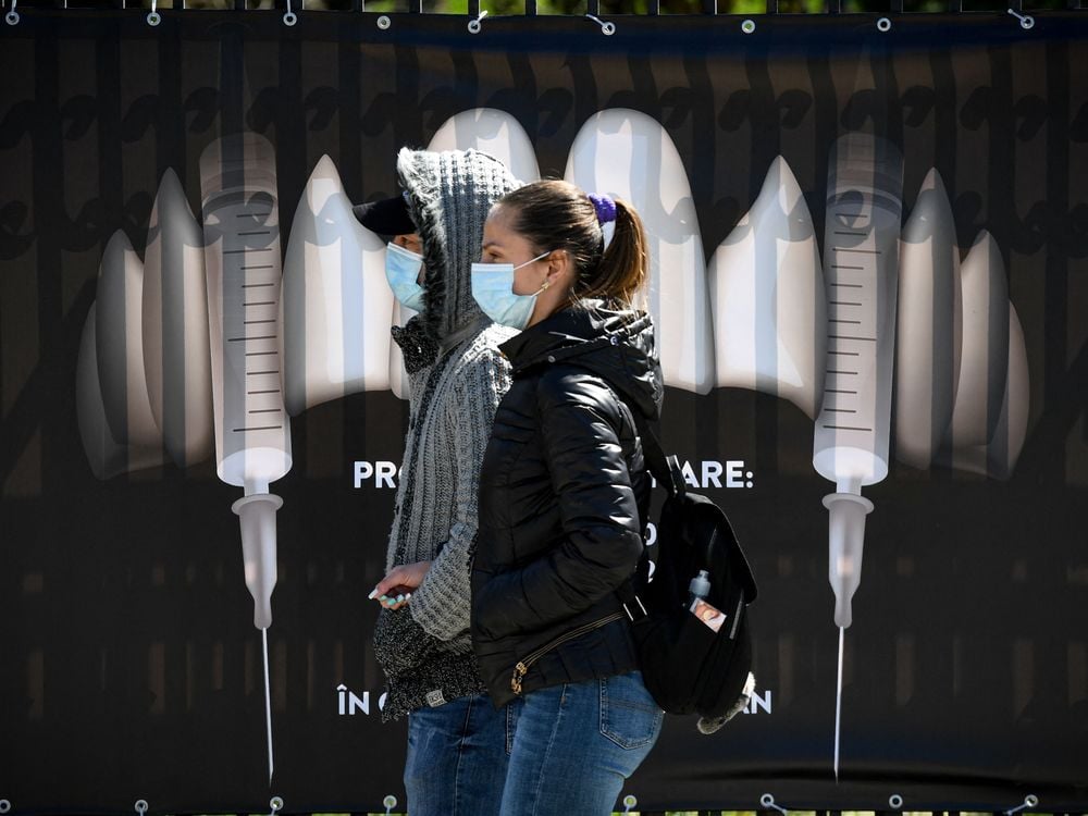 People wearing protection masks walk by a banner showing syringes as vampire fangs during the vaccination marathon organized at the "Bran Castle" in Bran village on May 8, 2021