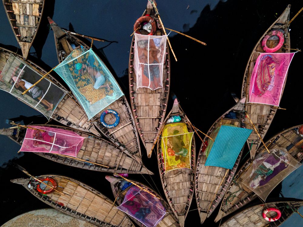 This photograph captures a moment of stillness in the restless heart of the river. The boatmen—after long hours of labor—lie asleep in their wooden boats, sheltered only by fragile mosquito nets. Their boats become both workplace and home, and the river becomes the only witness to their quiet dreams.

The colorful nets resemble floating cocoons, symbolizing how even in uncertainty, humans seek warmth, safety, and rest. Beneath this serene composition lies an unspoken truth: those who carry the weight of a city’s movement often sleep on waters that never rest.

Through this image, I aim to highlight the dignity, resilience, and poetic rhythm of lives lived close to nature yet far from privilege. It is a tribute to the invisible workforce who shape our everyday existence but remain hidden in society’s shadows.