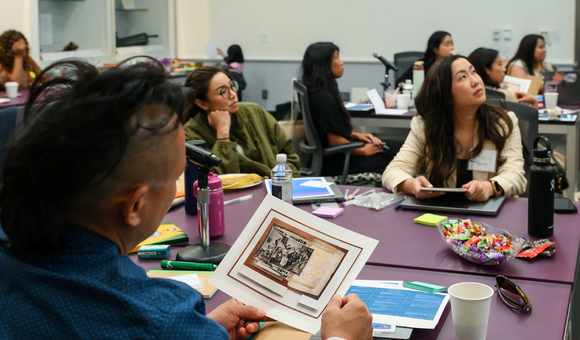 A man in a blue shirt looks at a photograph of archival images while several other people look toward a presentation
