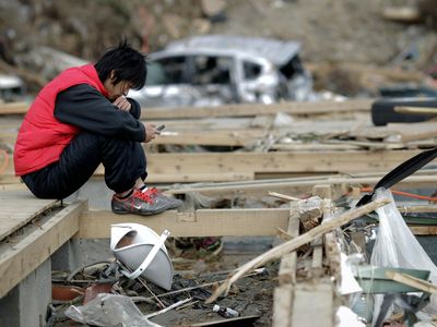 A man holds his mobile phone as he sits in the ruins of a house in Minamisanriku, Japan, after the area was devastated by a magnitude 9.0 earthquake and tsunami in March 2011.
