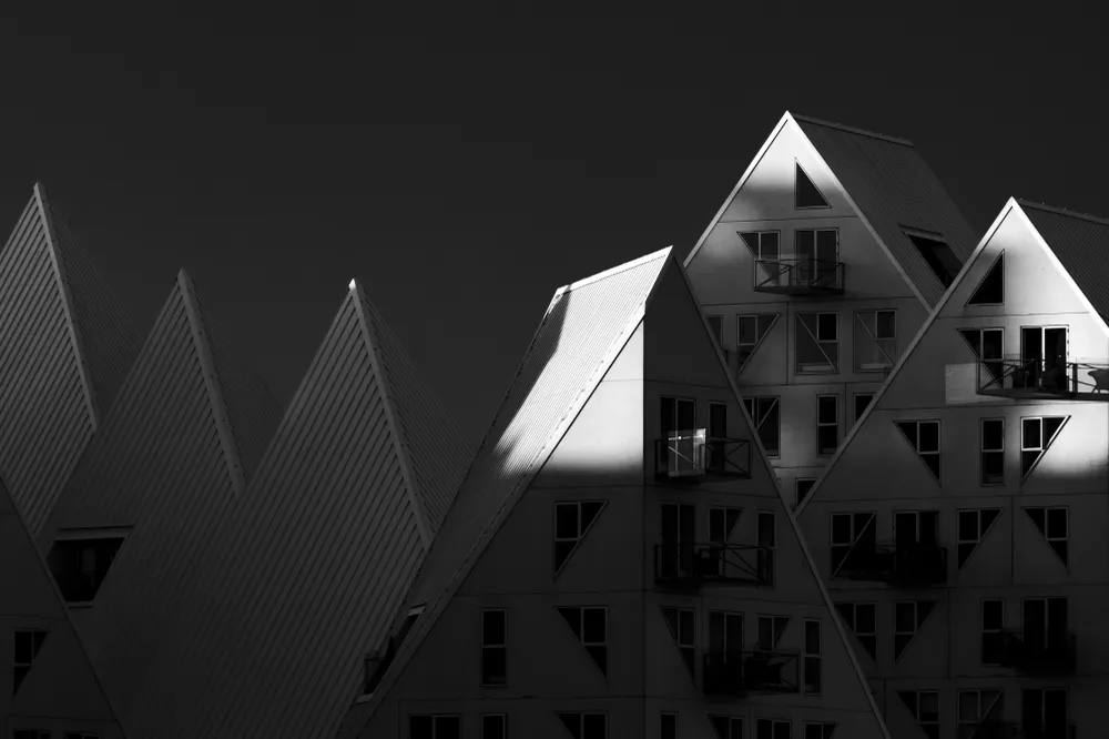 In the photo, the contrasts literally dance around the geometric shapes of the buildings, giving them a distinct character. Areas illuminated by the setting sun become bright focal points in contrast to the deep shadows, adding dynamism to the entire image.