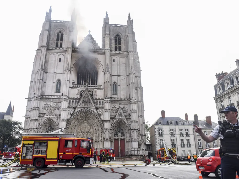 Cathedral in Nantes with black smoke, a firefighter's truck in the foreground