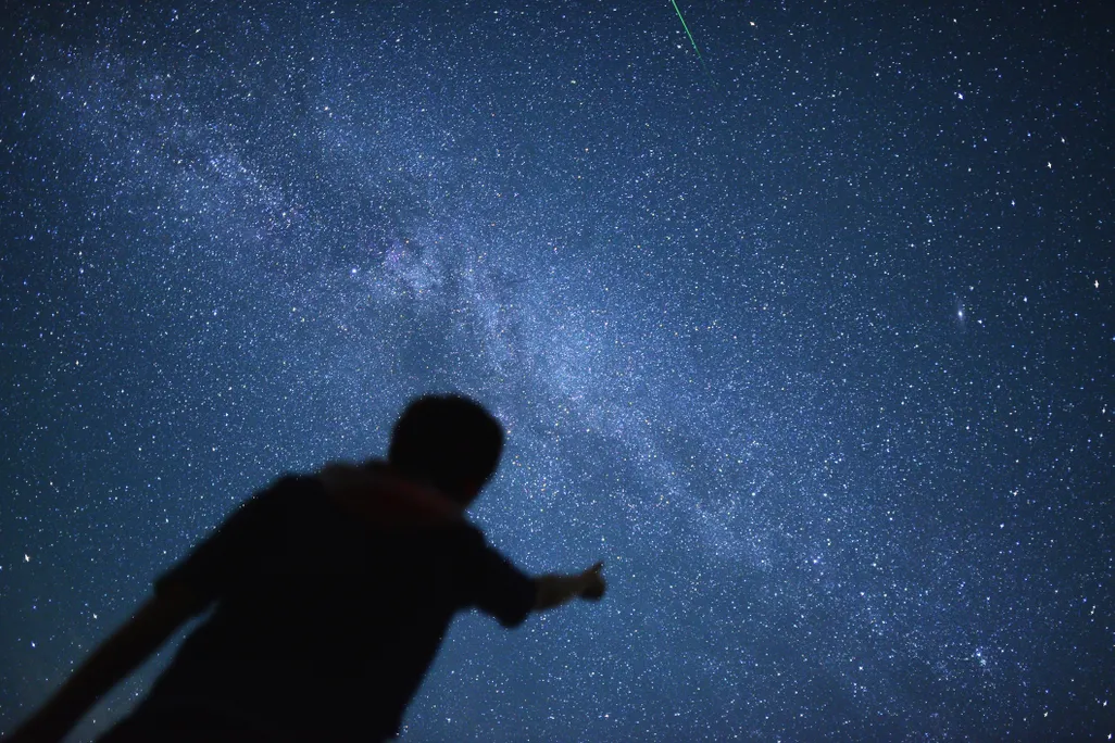 silhouette of a person pointing up at a starry sky