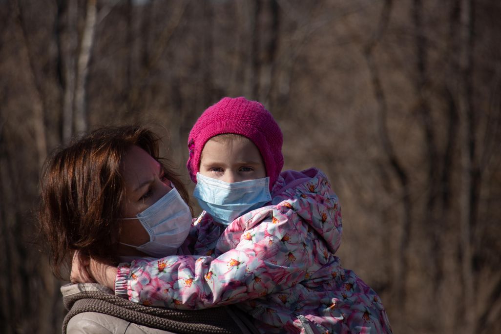 A photo of a woman holding a small child in her arms. Both are wearing masks.