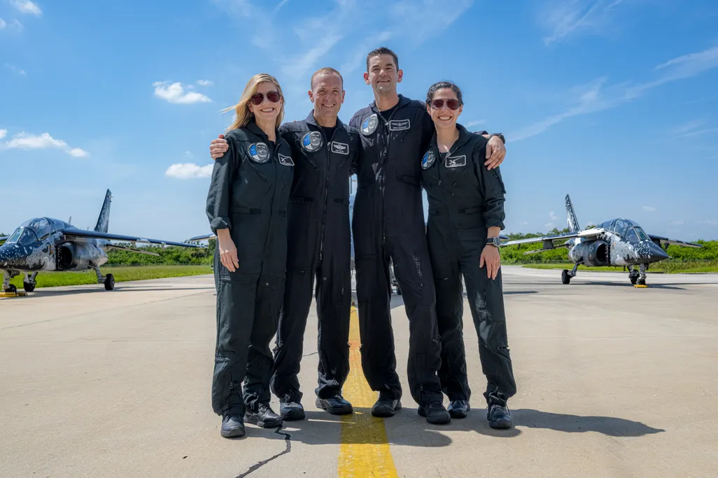 Four people in blue suits stand on a runway