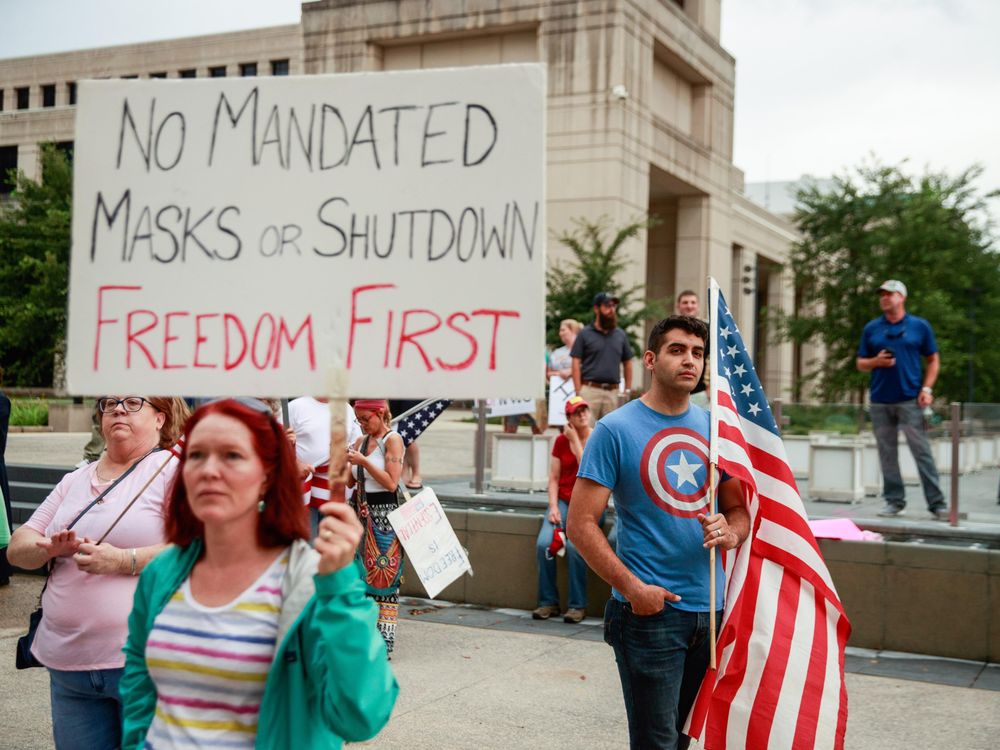 At an anti-mask rally, a protester holds a placard saying No Mandated Masks or Shutdown Freedom First 