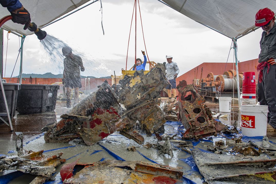 Team members clean and inspect recovered wreckage identified as part of the plane’s fuselage. Any human remains and personal belongings discovered will be repatriated to the United States. The plane’s wreckage, however, will ultimately be returned to the