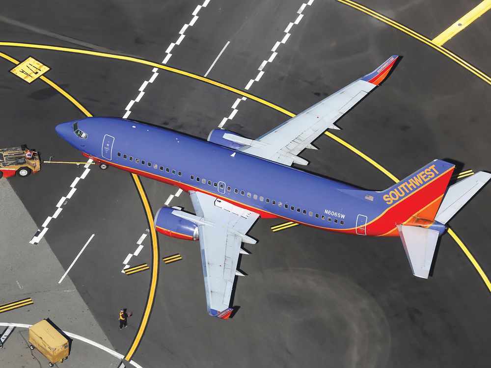 A twin-engine jet airliner painted in a livery of purple, red, and orange is parked on an airport ramp. The tail of the airline is marked with the word “Southwest.”