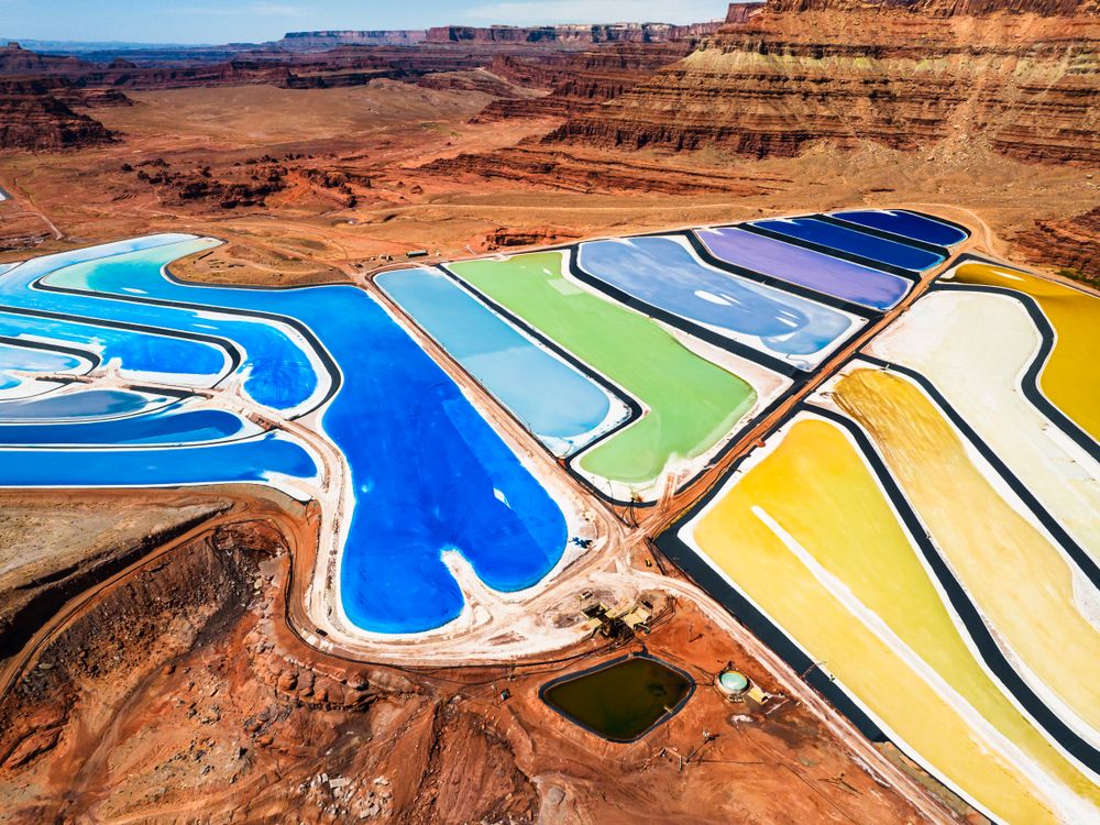 In the heart of the canyonlands, a mineral mine weaves a striking industrial tapestry. Its vivid evaporation ponds stand out as a colorful mosaic against the stark, red earth, showcasing a blend of raw natural beauty and human innovation.