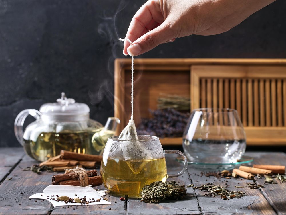 Hand holding tea bag by string over hot cup of tea