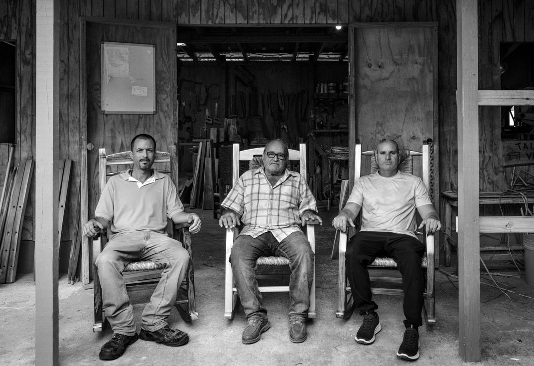 a black and white photograph of three men sitting in rocking chairs on a porch