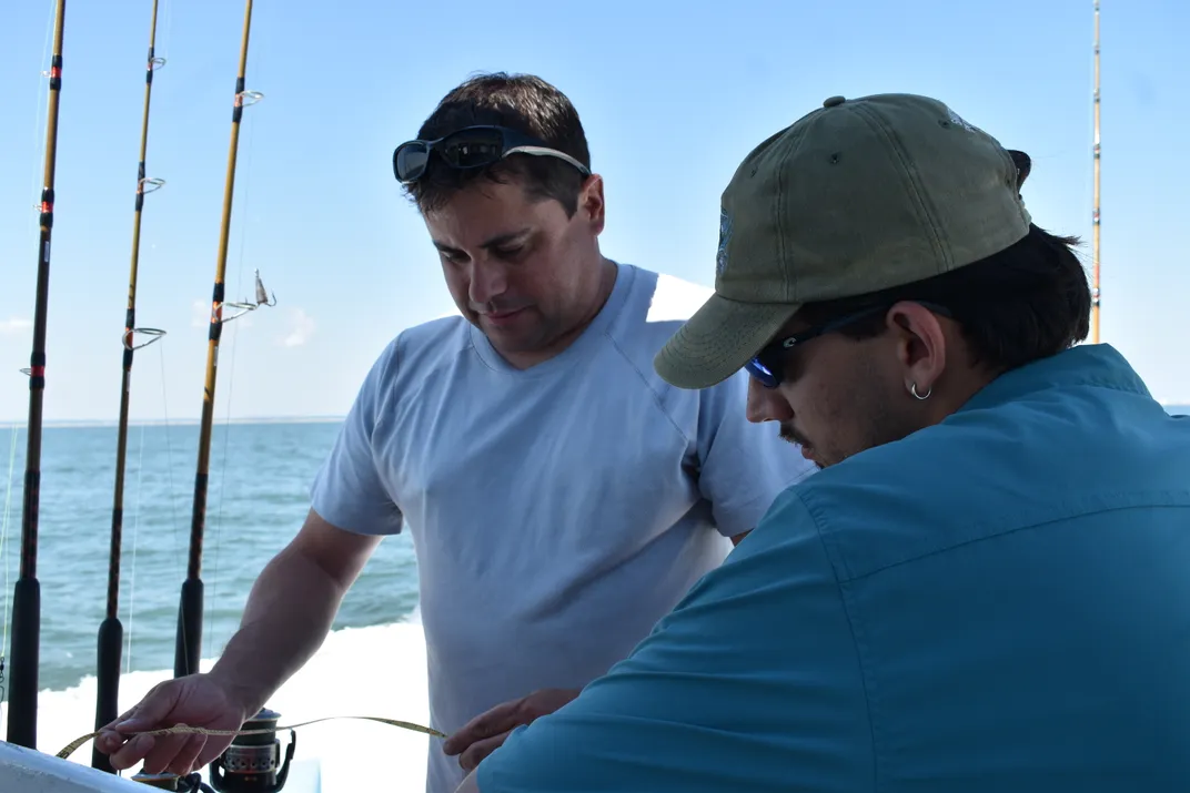 two men on a boat look at notes with fishing rods beside them