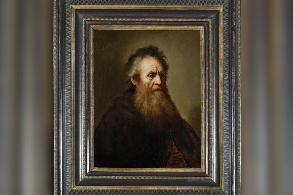 A portrait in a gilt frame of an elderly man with a scraggly beard, graying hair and wearing a simple dark garment