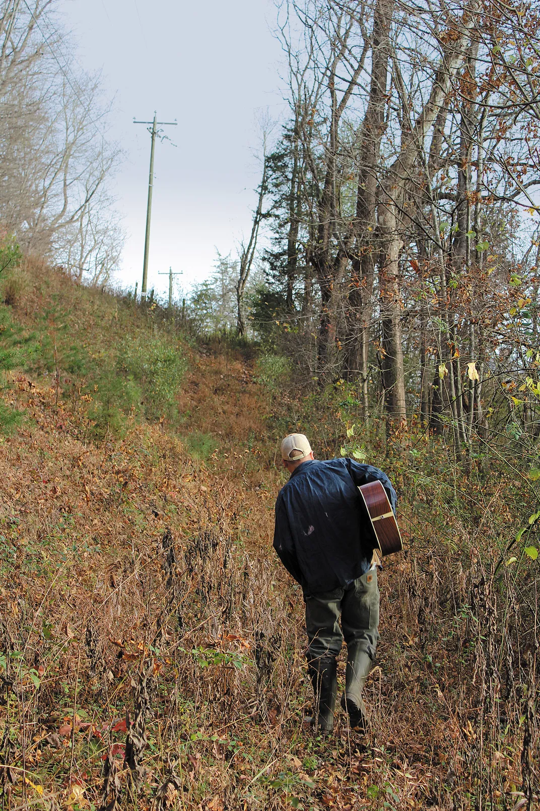 a man walks in the woods carrying his guitar