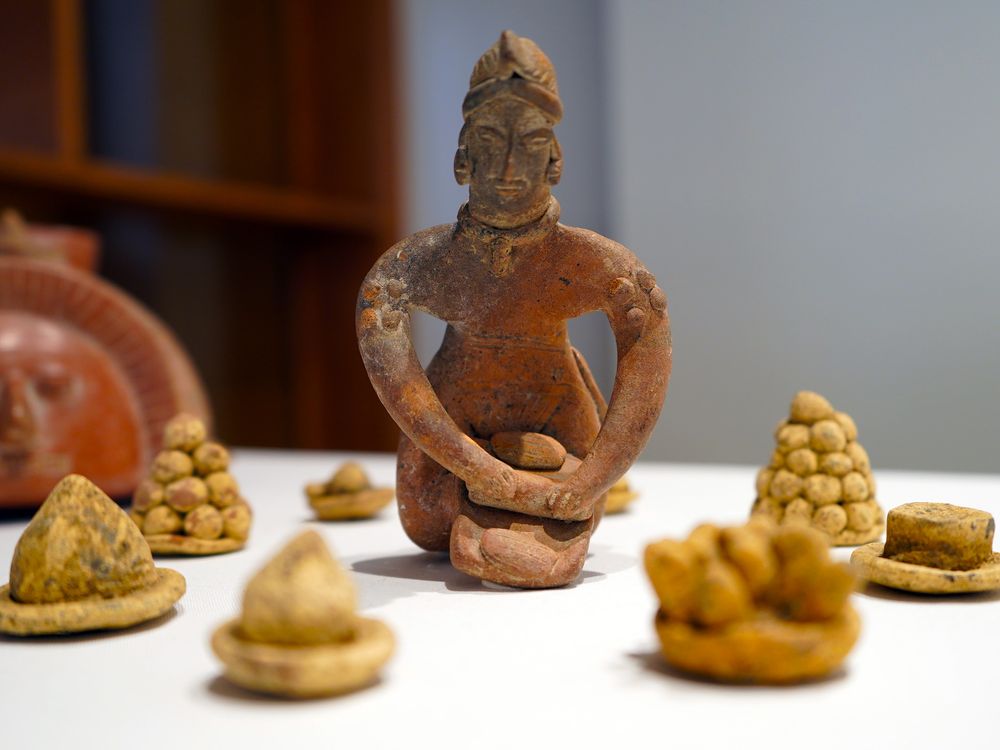 Statuette of figure rolling dough on board surrounded by miniature corn sculptures