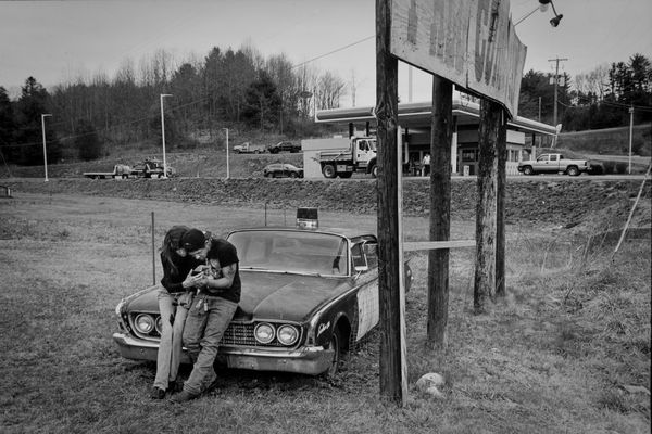 Young couple sitting on hood of old police car. thumbnail