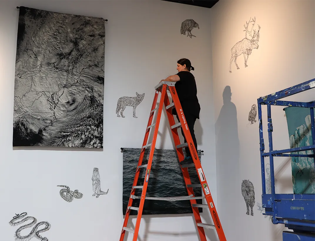 Artist on a ladder hanging art on a white wall