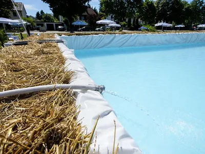 Water runs from a hose into a hay bale pool.