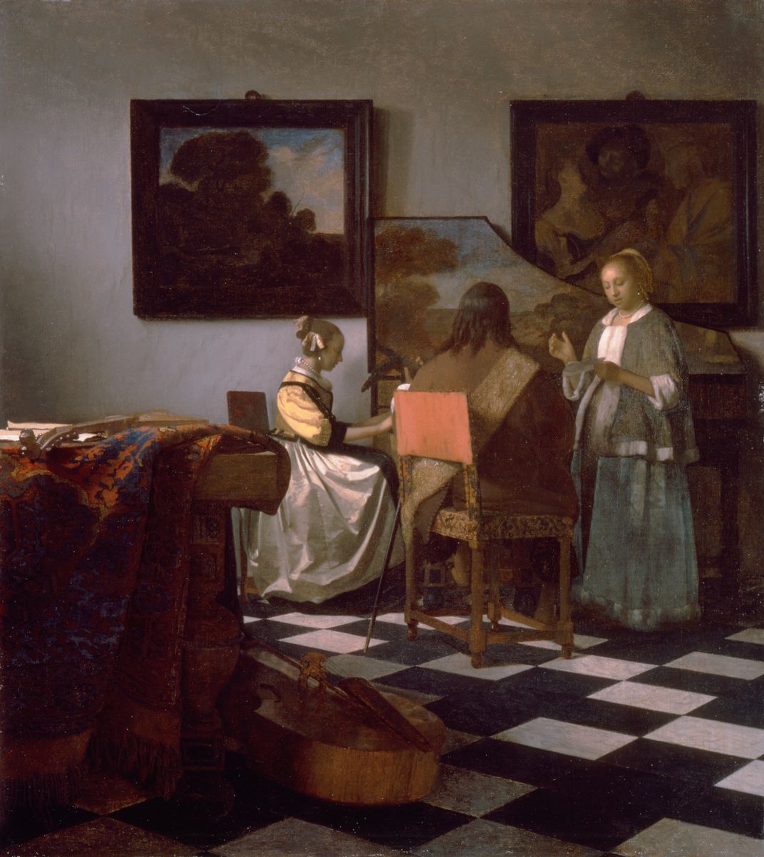 A young girl sits at a piano and practices in a stately room with a black and white checkered floor and canvases on the walls