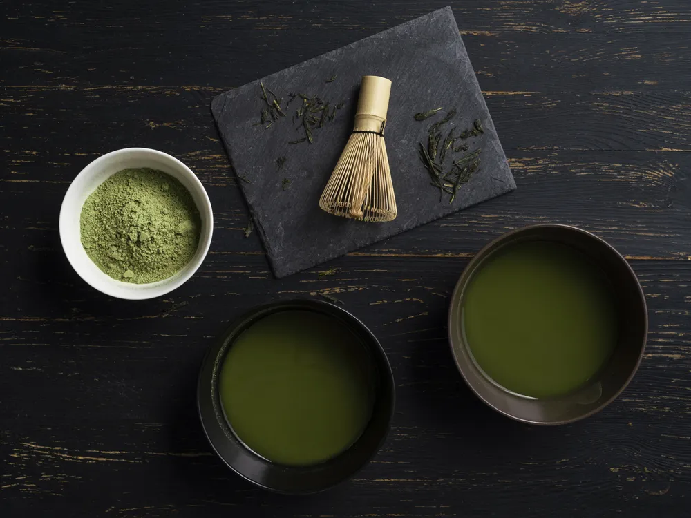 A whisk and bowls of matcha tea and tea powder
