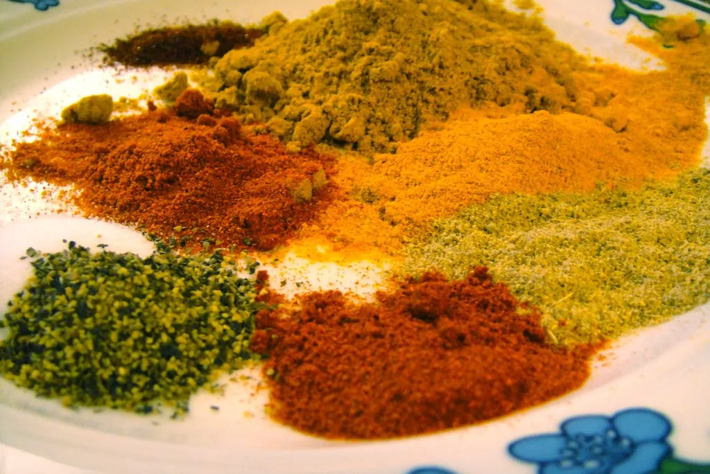 piles of red, brown, orange and yellow spices on a white plate with blue flowers around the rim