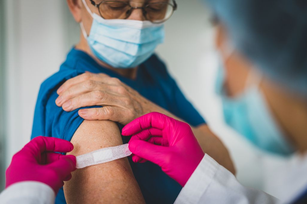 A doctor with pink gloves applies a bandaid to an older woman's arm