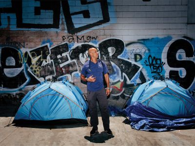 man standing in front of two blue tents and a wall of graffiti