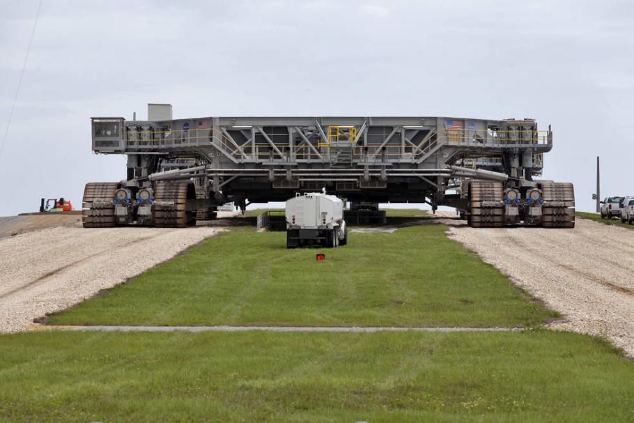 Giant crawler transporter on roadway. A truck is visible in front of the crawler.