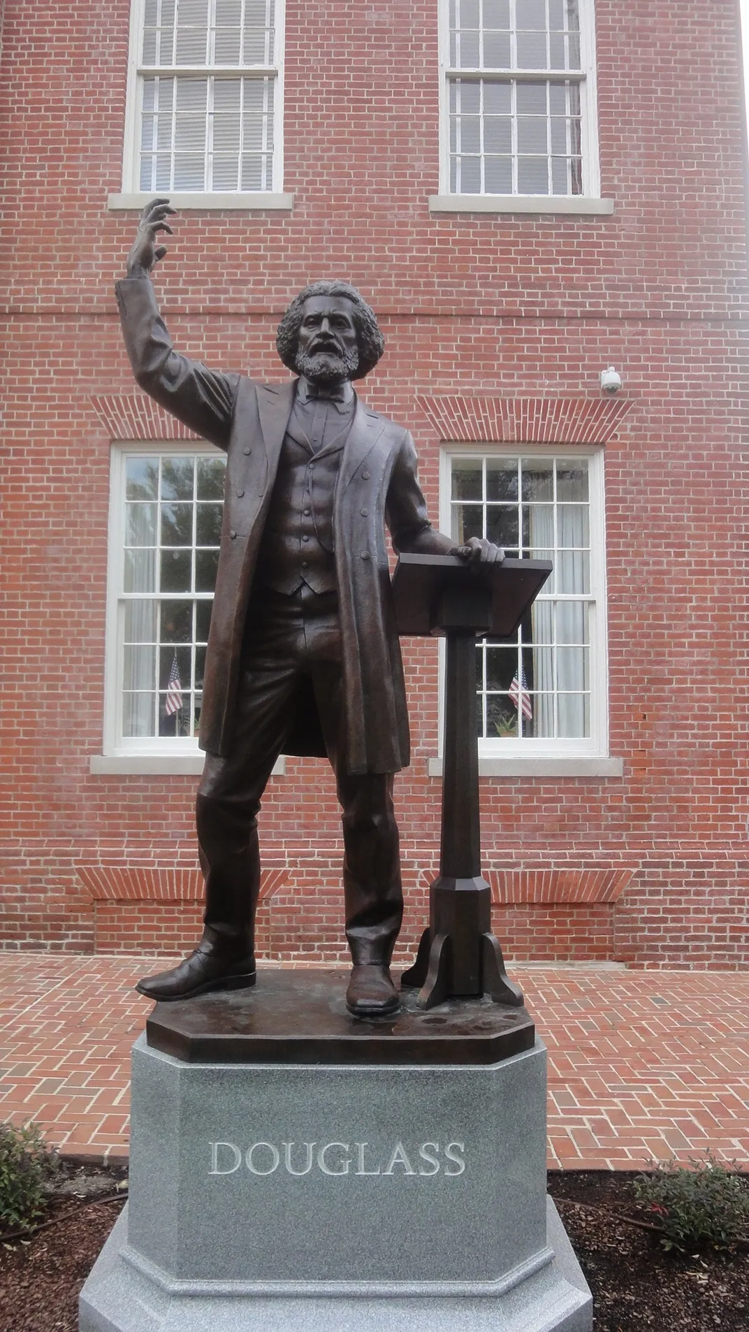 A statue of Frederick Douglass standing near a podium, with one hand lifted as though delivering a great speech
