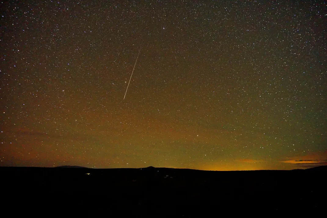 a meteor streaks through an orange-tinted sky