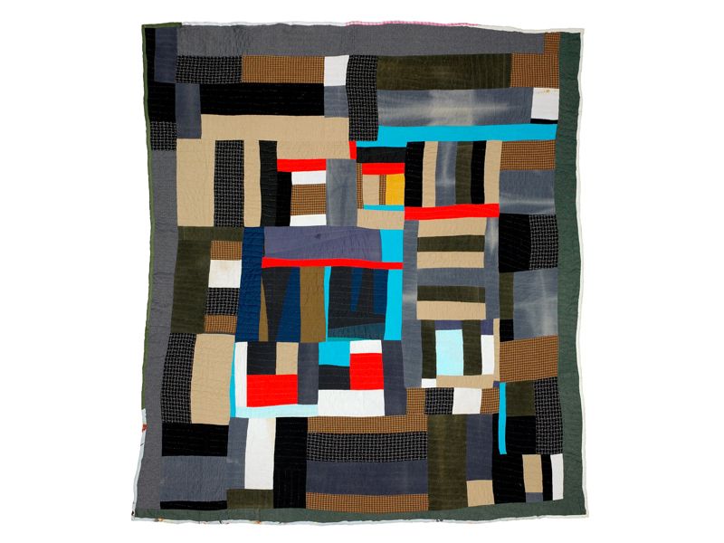 A quilt made of interlocking rectangles of dark green, gray, tan, with bright spots of light cyan, red and a tiny bit of yellow at the center