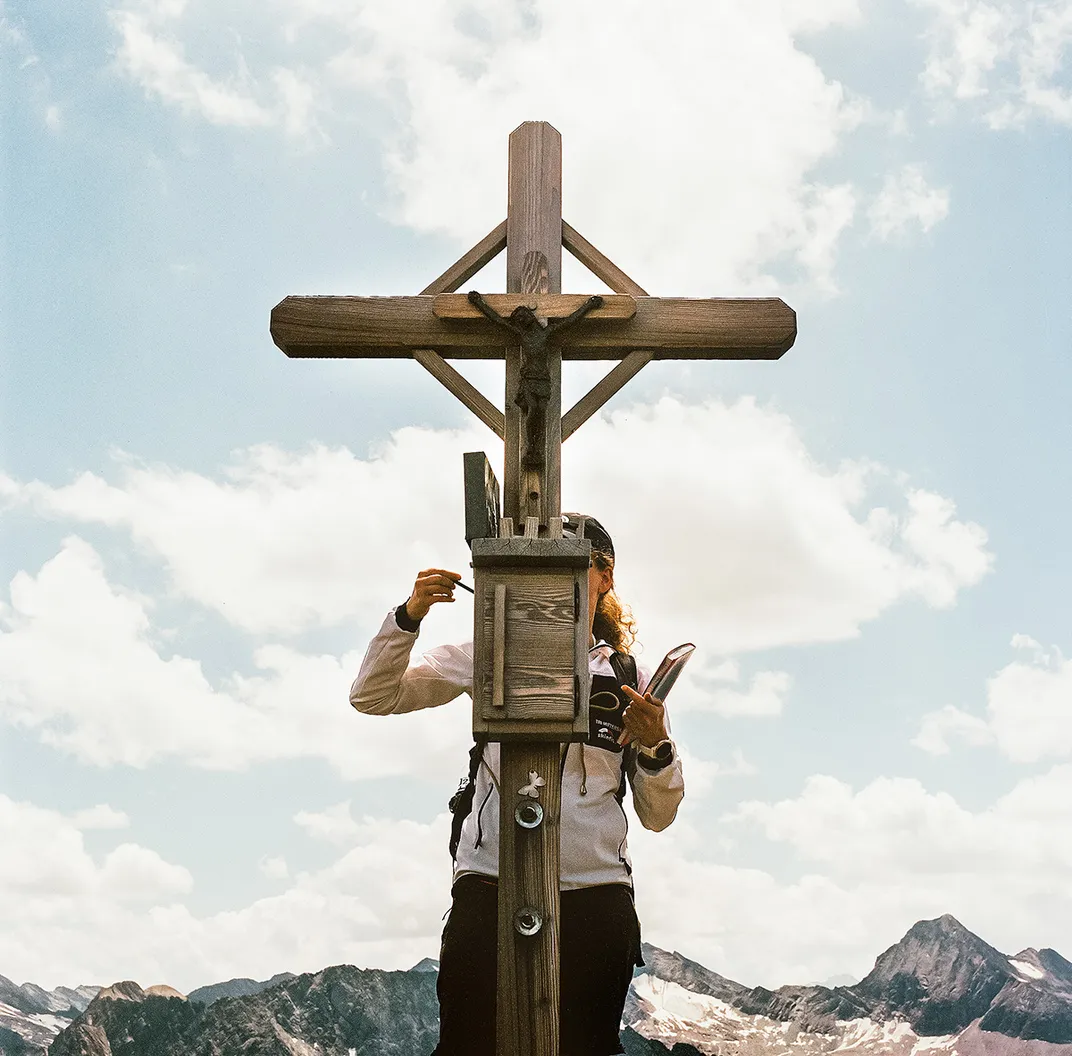 A hiker signs the summit register below the summit cross at the top of Krimml Pass.