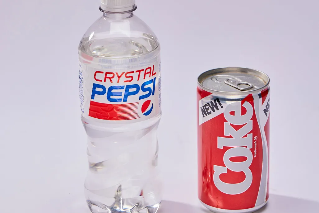Bottle of clear Crystal Pepsi next to can of New Coke