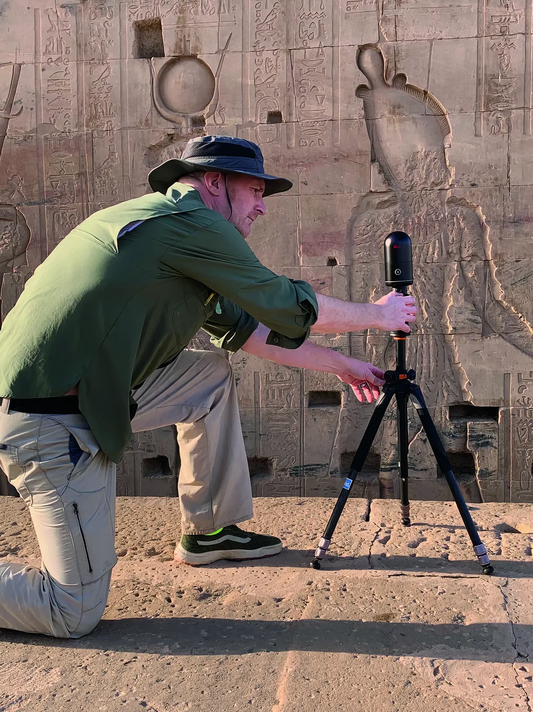 a man using a camera on tripod taking photos of ancient graffiti