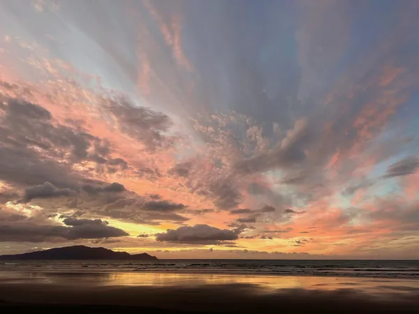 Pink clouds at sunset reflect in the sand of Te Horo Beach, New Zealand. thumbnail