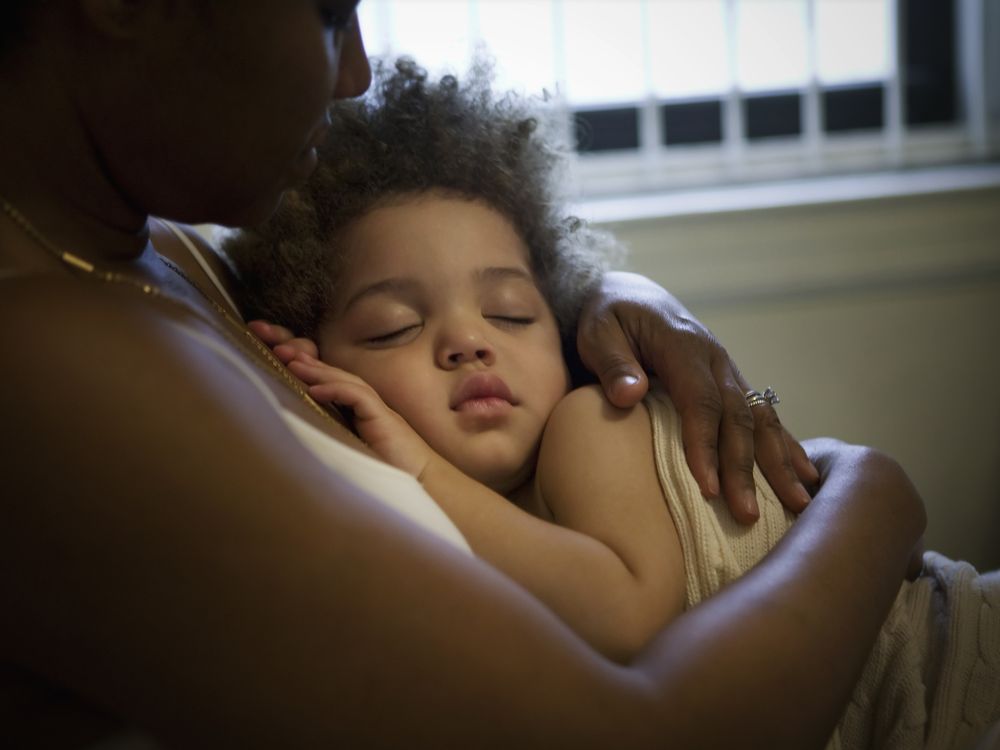 A sitting mother holds a sleeping child to her chest